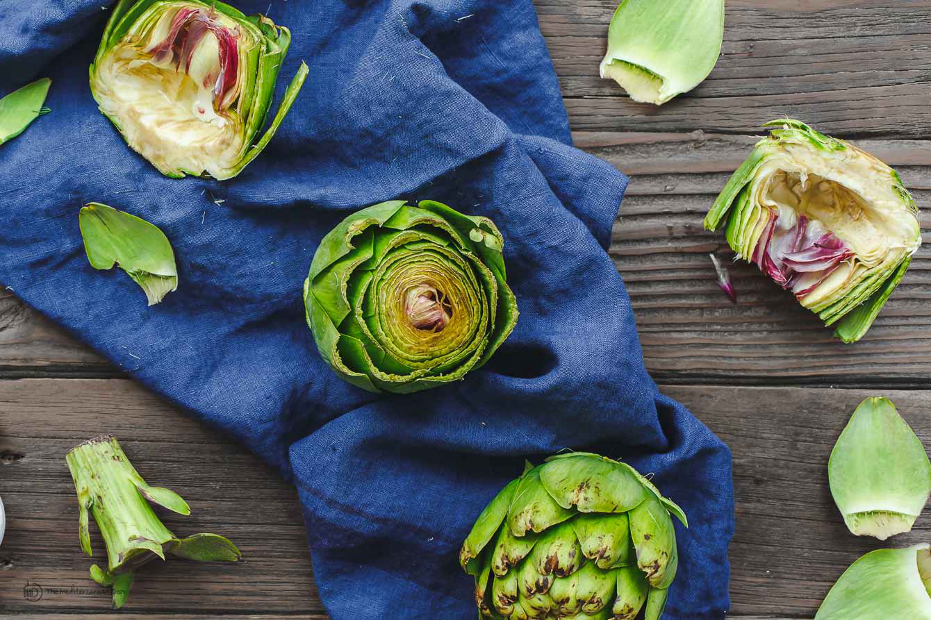 artichoke. One artichoke halved and cleaned and two whole artichokes next to it