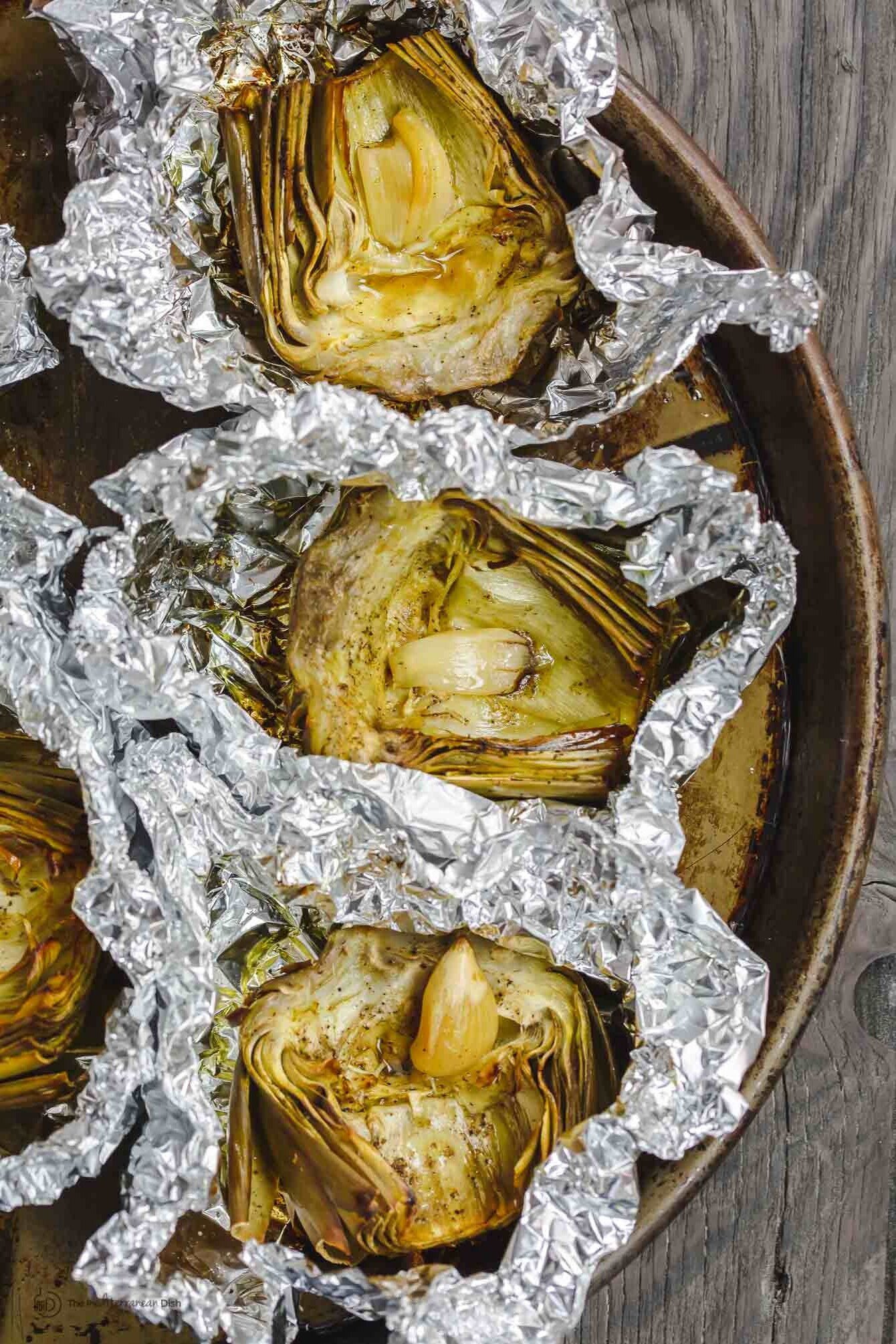 roasted artichoke halves in foil with garlic in the middle