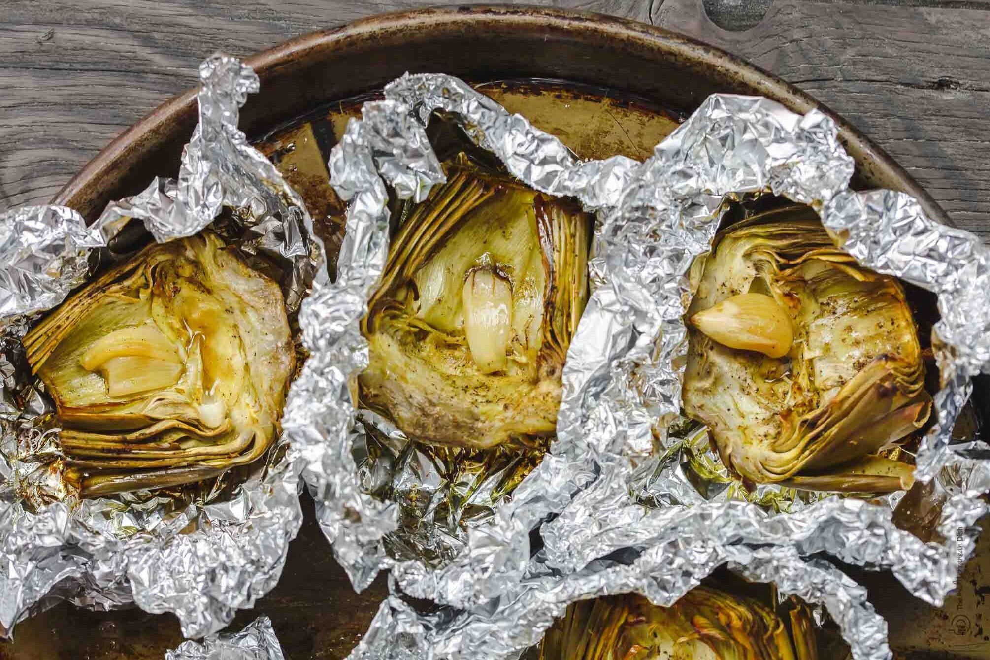 roasted artichoke halves in foil with garlic in the middle