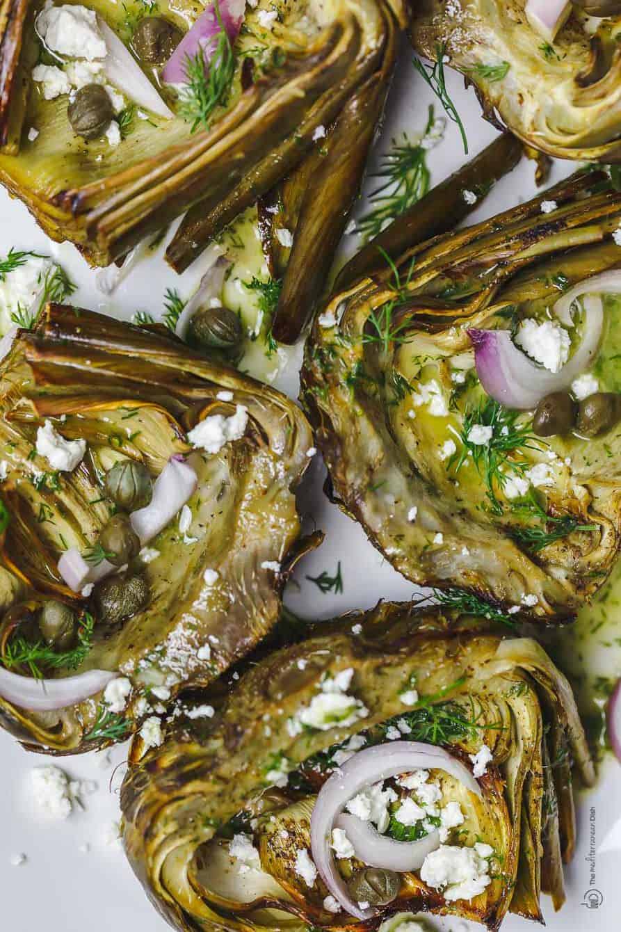 Mediterranean-style roasted artichokes topped with shallots, feta, capers, and dill