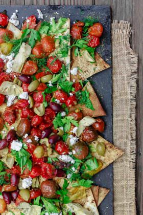 Mediterranean Roasted Tomato Nachos Recipe | The Mediterranean Dish. Homemade crispy nachos made with light, healthy flatbread. Loads of garlic roasted tomatoes and Mediterranean favorites on top! The perfect appetizer or little mezze dish!