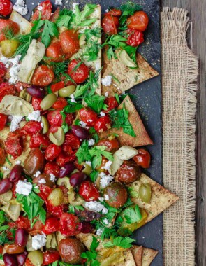 Mediterranean Roasted Tomato Nachos Recipe | The Mediterranean Dish. Homemade crispy nachos made with light, healthy flatbread. Loads of garlic roasted tomatoes and Mediterranean favorites on top! The perfect appetizer or little mezze dish!