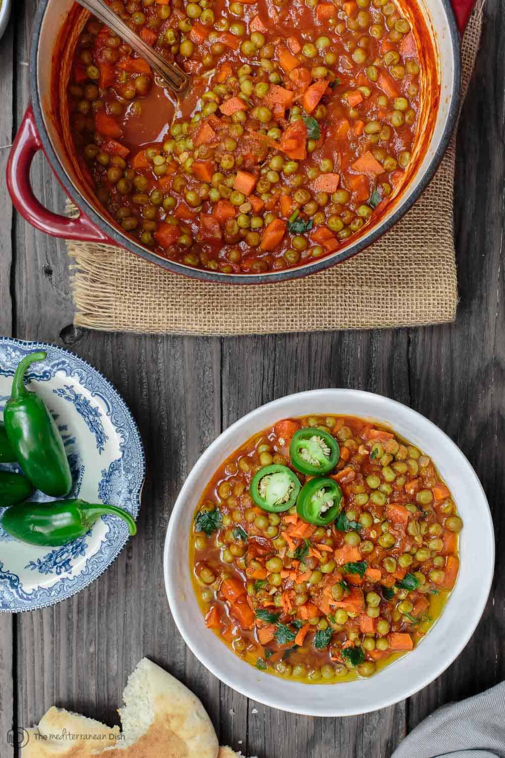 Pot of stew ready for serving with a side of jalapeno peppers and bread