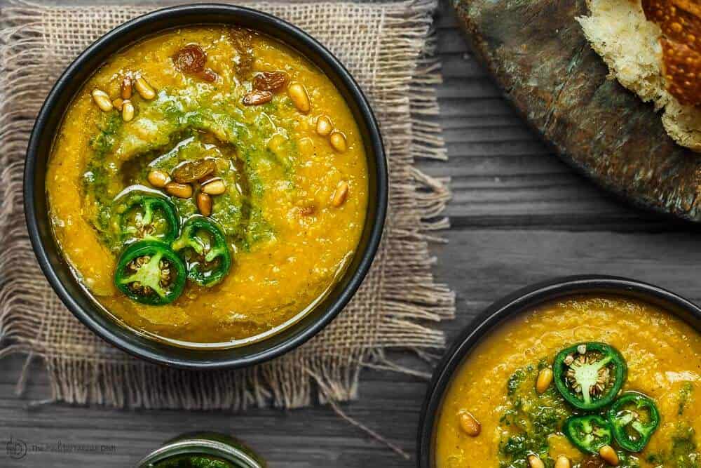 Two bowls of vegan pumpkin soup with a side of crust bread
