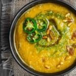 Vegan Pumpkin Soup in serving bowl. Topped with spicy cilantro pesto and jalapenos