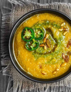 Vegan Pumpkin Soup in serving bowl. Topped with spicy cilantro pesto and jalapenos