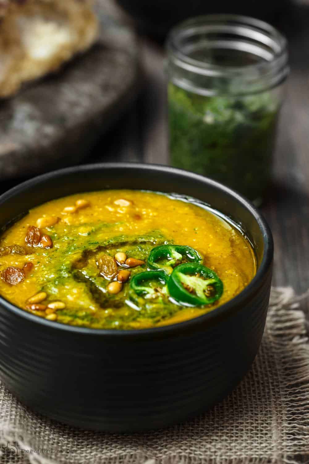 Vegan Lentil Pumpkin Soup in bowl. A jar of spicy cilantro pesto to the side