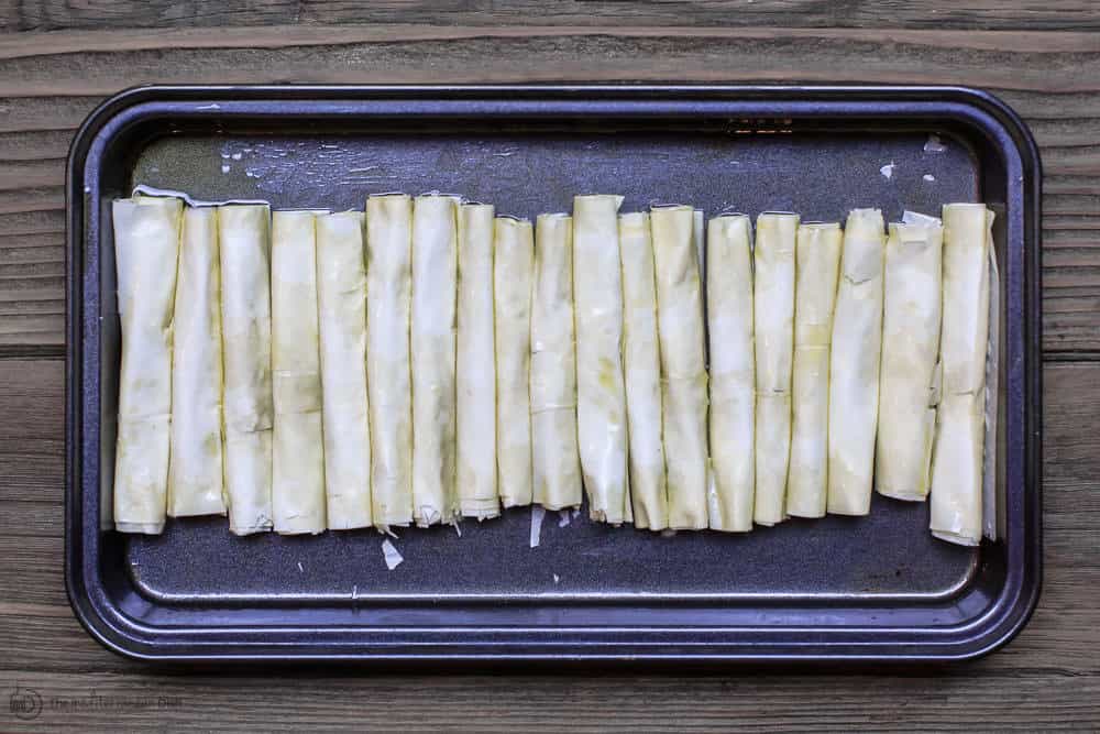 Filled rolls lined in a row in a baking pan