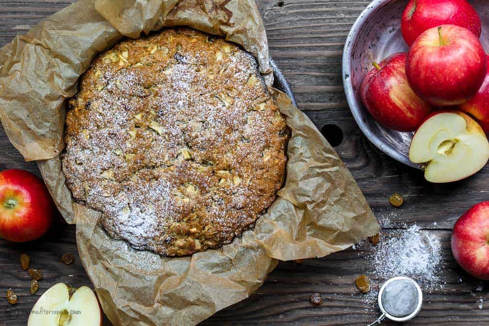 Olive Oil Cake In Pan with Parchment Paper. A bowl of apples on side