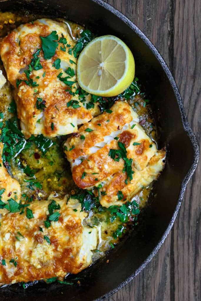 Baked cod recipe with lemon and garlic, served on a cast-iron skillet