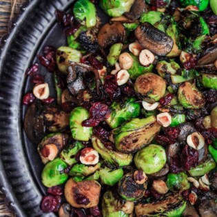 Olive Oil Fried Brussels Sprouts | The Mediterranean Dish. Simple olive oil fried sprouts with mushrooms, cranberries, and hazelnuts, makes a festive vegan and gluten free side dish. See full recipe on TheMediterraneanDish.com #mediterraneanrecipe #friedbrusselssprouts #brusselssprouts #thanskgivingdinner #holidaysidedish #sidedish