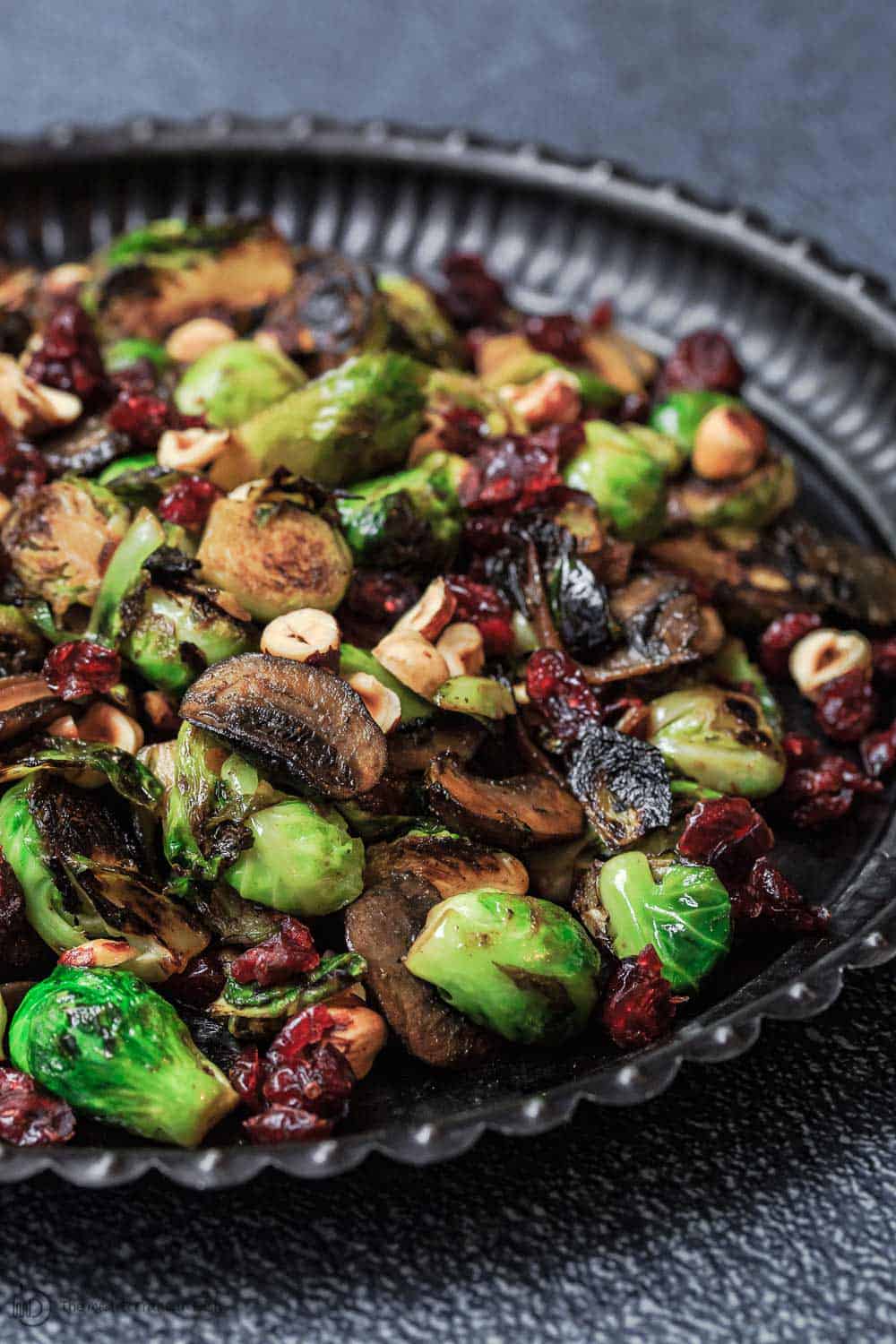 Olive Oil Fried Brussels Sprouts | The Mediterranean Dish. Simple olive oil fried sprouts with mushrooms, cranberries, and hazelnuts, makes a festive vegan and gluten free side dish. See full recipe on TheMediterraneanDish.com #mediterraneanrecipe #friedbrusselssprouts #brusselssprouts #thanskgivingdinner #holidaysidedish #sidedish