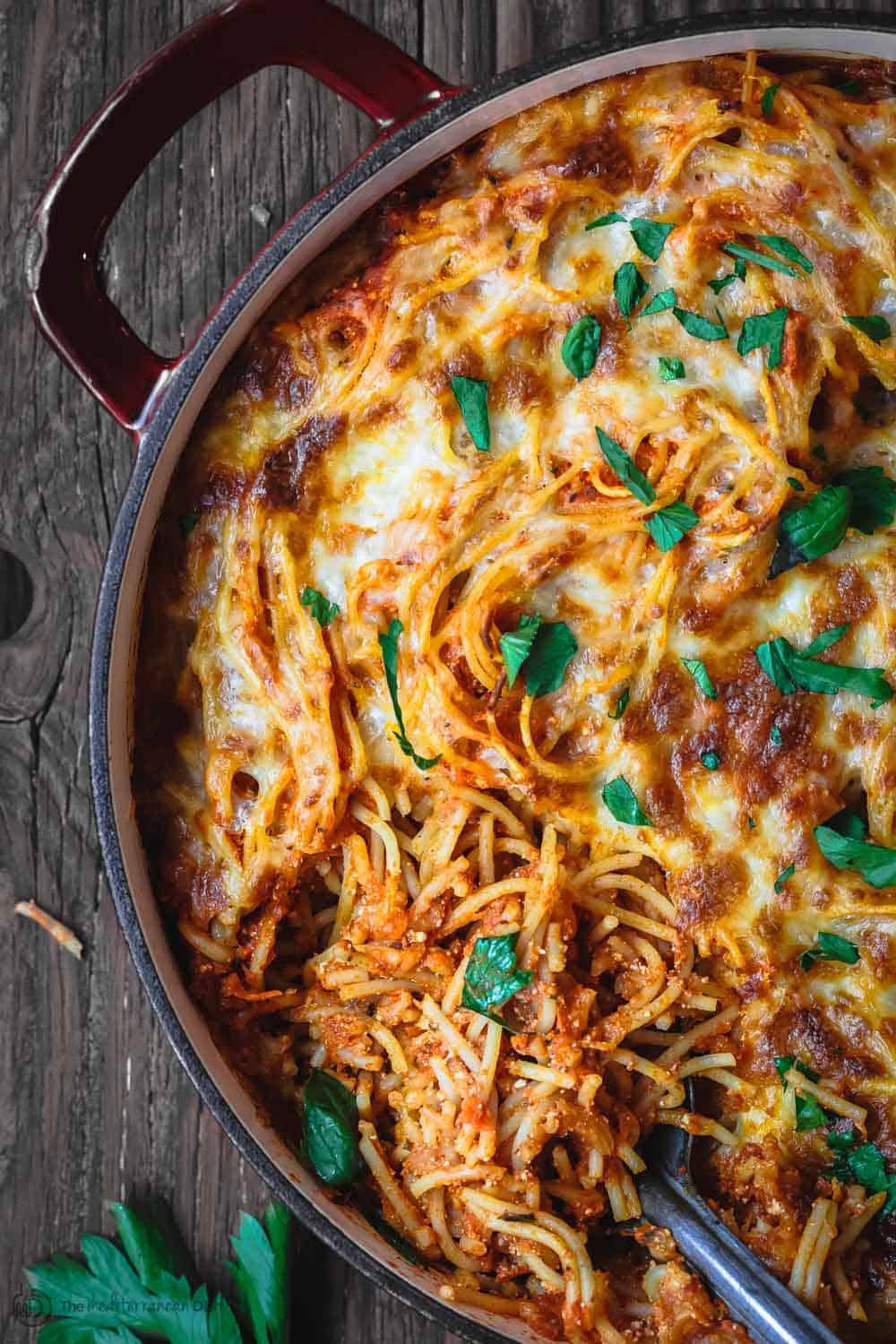 Baked spaghetti garnished with fresh basil and parsley.