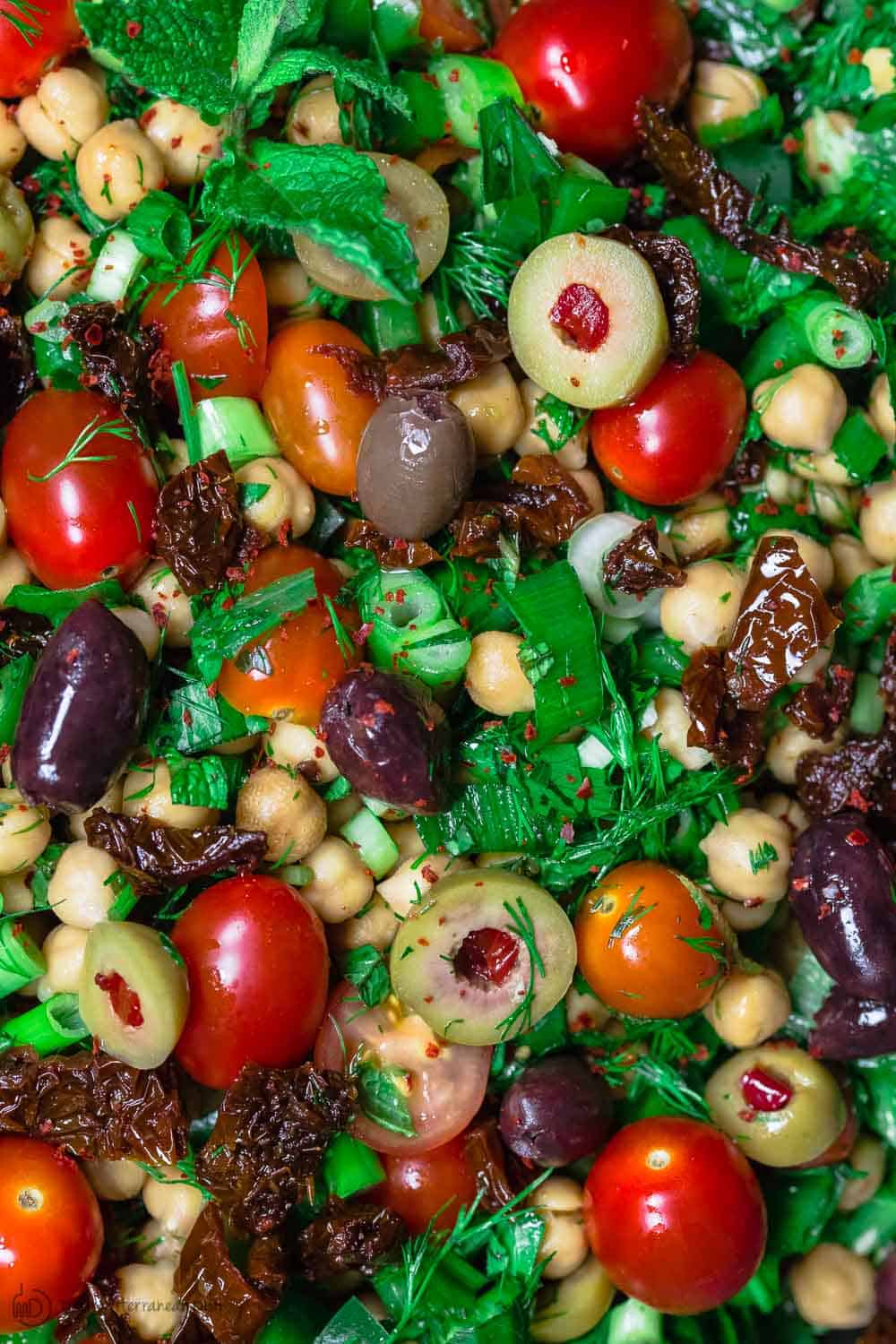 A close up photo of balela salad with fresh. herbs, tomatoes, and olives