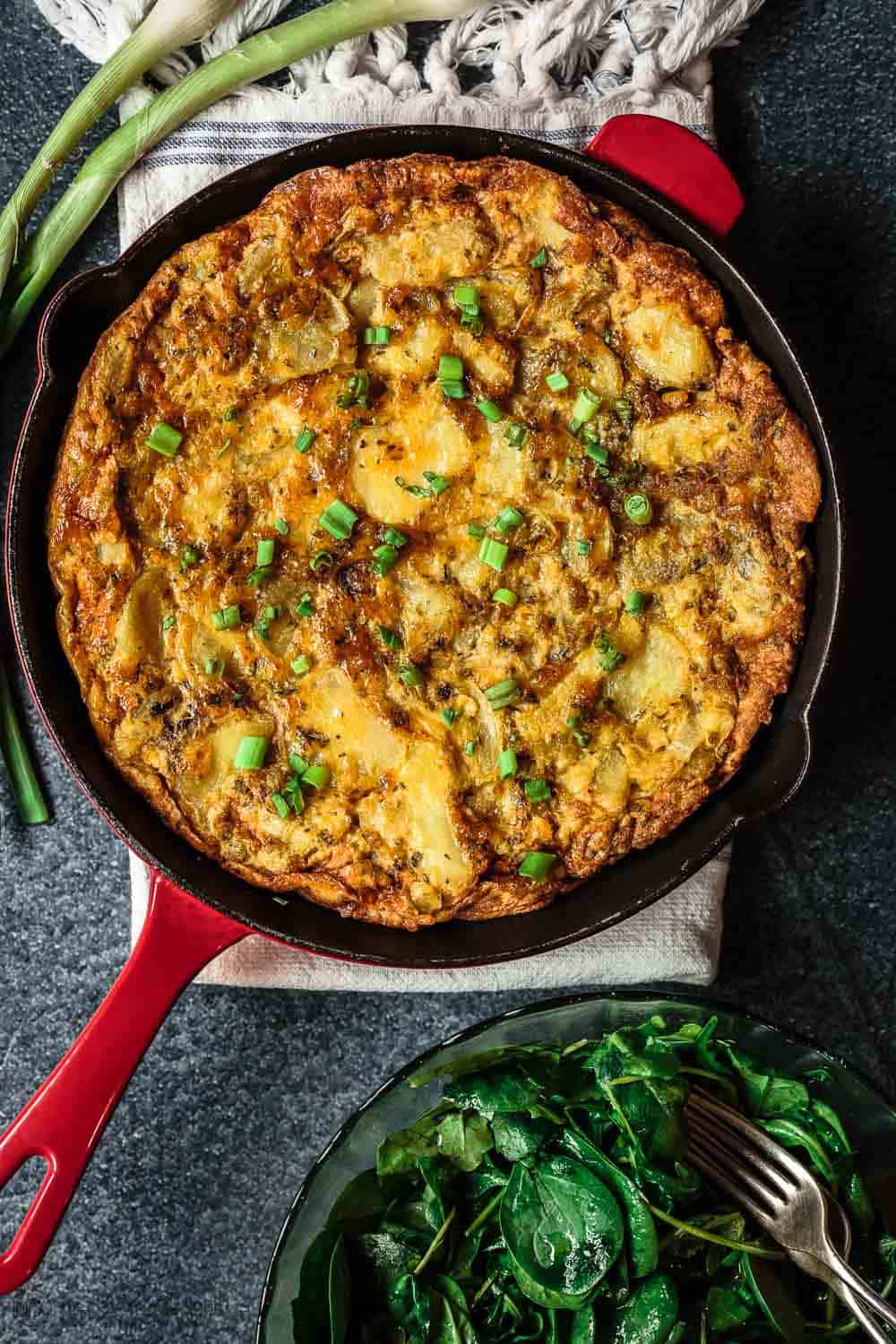 Spanish Tortilla in Skillet served with a Side of Arugula Salad and Spring onions for garnish