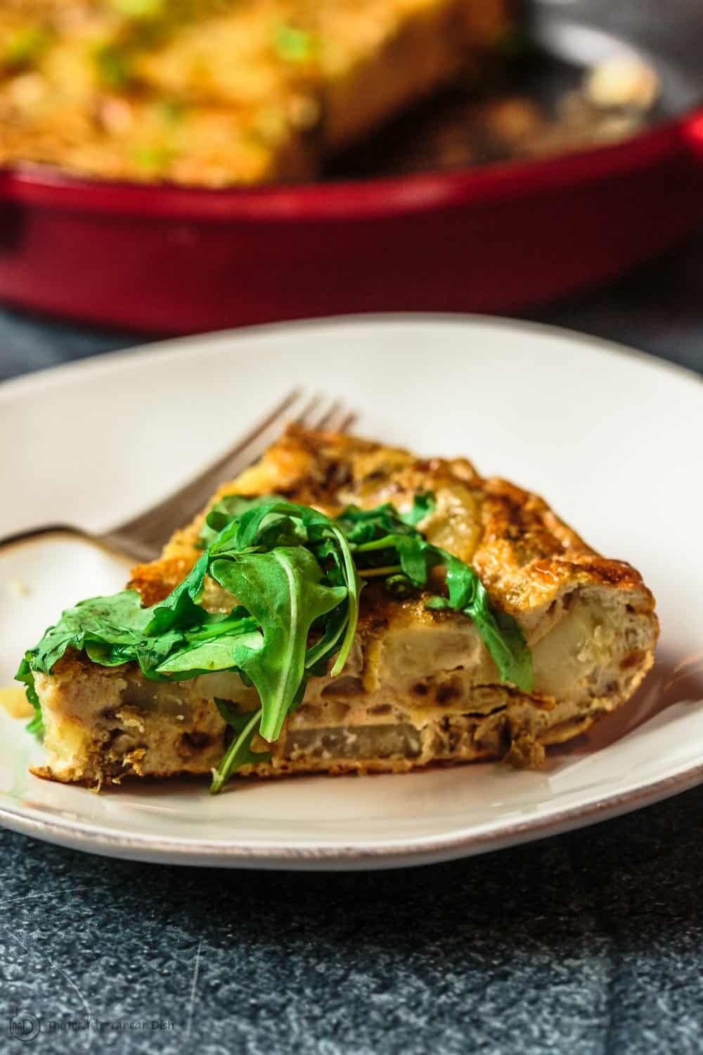 One slice of spanish omellete on a plate with a bit of arugula