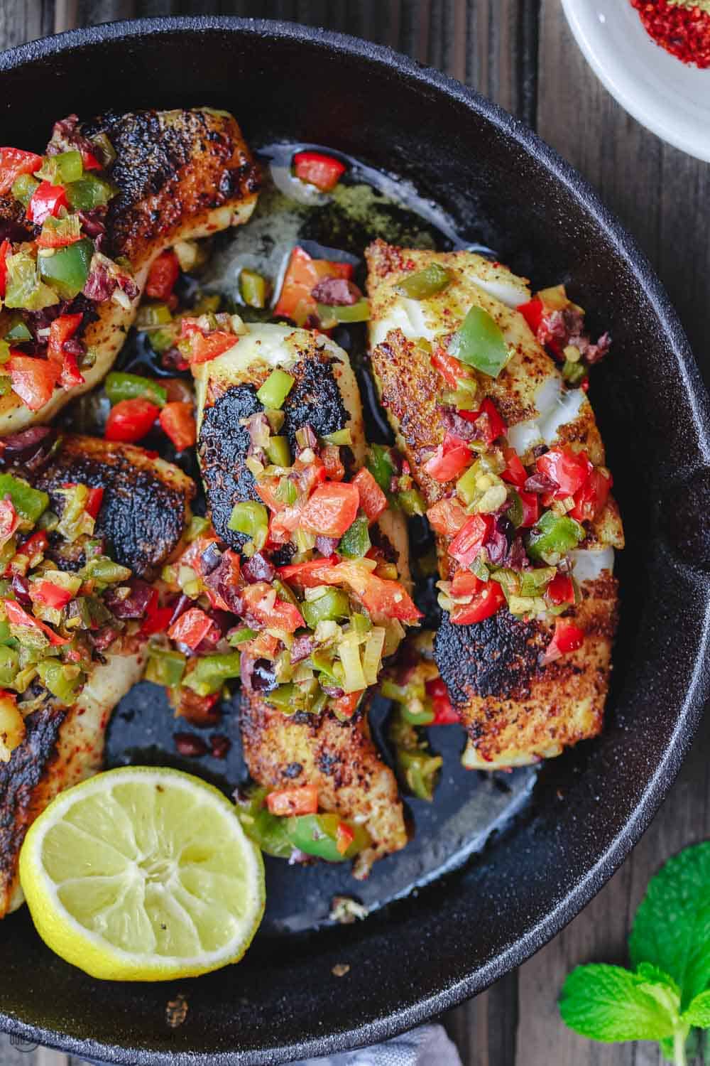 A cast iron skillet with pan seared sea bass served with a bell pepper medley on top