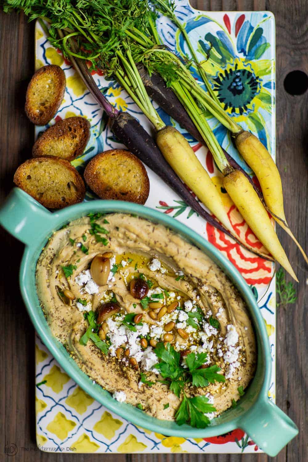 Plate of roasted garlic hummus garnished with olive oil and parsley. Served with a side of toast.