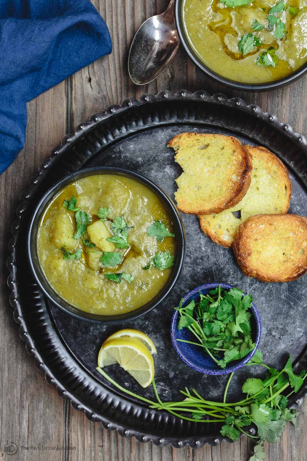 Serving tray containing a bowl of soup, lemon wedges, extra garnish and toasted bread