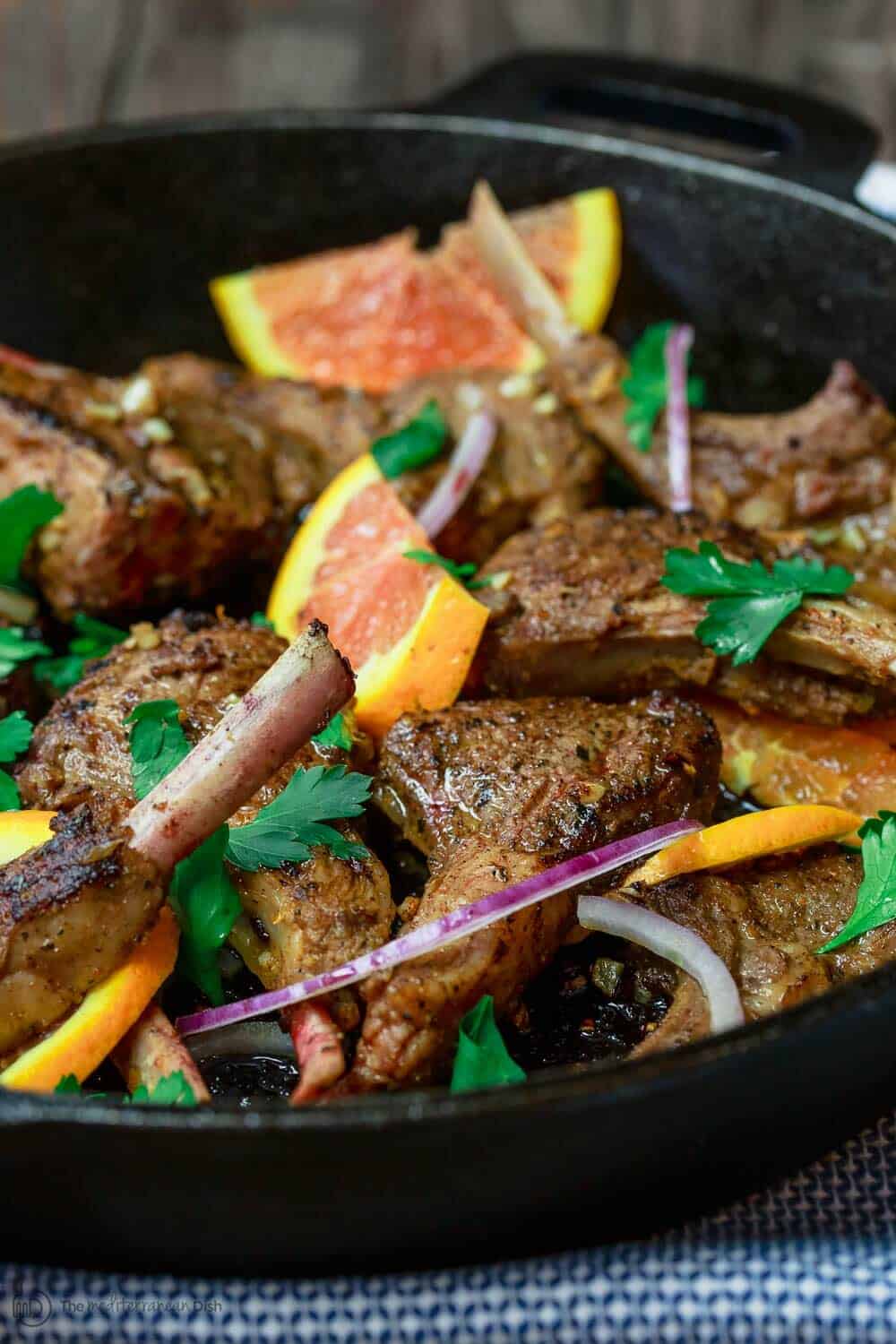 Orange Harissa Lamb Chops, cooked in skillet. Garnish with orange slices and red onion
