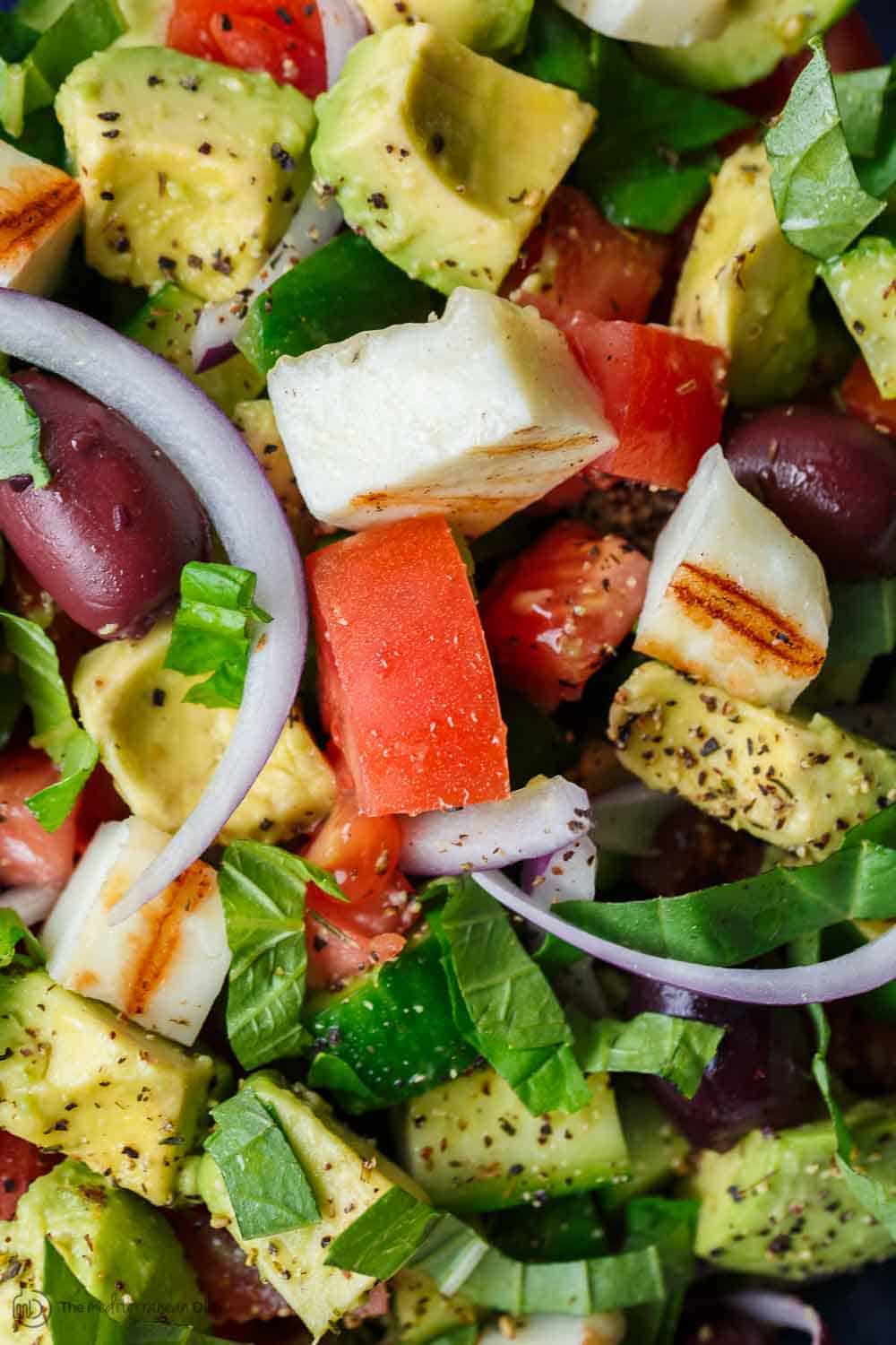 Simple Mediterranean Avocado Salad | The Mediterranean Dish. The BEST avocado salad, prepared Mediterranean style with tomatoes, cucumbers and a the perfect garlic vinaigrette! Use grilled halloumi cheese for croutons, or leave them out for a vegan option. #avocado #avocadosalad #mediterraneandiet #mediterraneanfood #salad #avocados #vegetarianrecipes #glutenfree