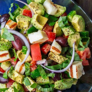 Simple Mediterranean Avocado Salad | The Mediterranean Dish. The BEST avocado salad, prepared Mediterranean style with tomatoes, cucumbers and a the perfect garlic vinaigrette! Use grilled halloumi cheese for croutons, or leave them out for a vegan option. #avocado #avocadosalad #mediterraneandiet #mediterraneanfood #salad #avocados #vegetarianrecipes #glutenfree