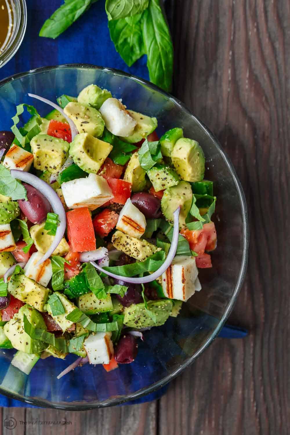 Simple Mediterranean Avocado Salad | The Mediterranean Dish. The BEST avocado salad, prepared Mediterranean style with tomatoes, cucumbers and a the perfect garlic vinaigrette! Use grilled halloumi cheese for croutons, or leave them out for a vegan option. #avocado #avocadosalad #mediterraneandiet #mediterraneanfood #salad #avocados #vegetarianrecipes #glutenfree