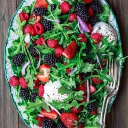 Arugula salad with burrata cheese, raspberries, strawberries and blackberries served in a large plate