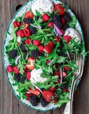 Arugula salad with burrata cheese, raspberries, strawberries and blackberries served in a large plate