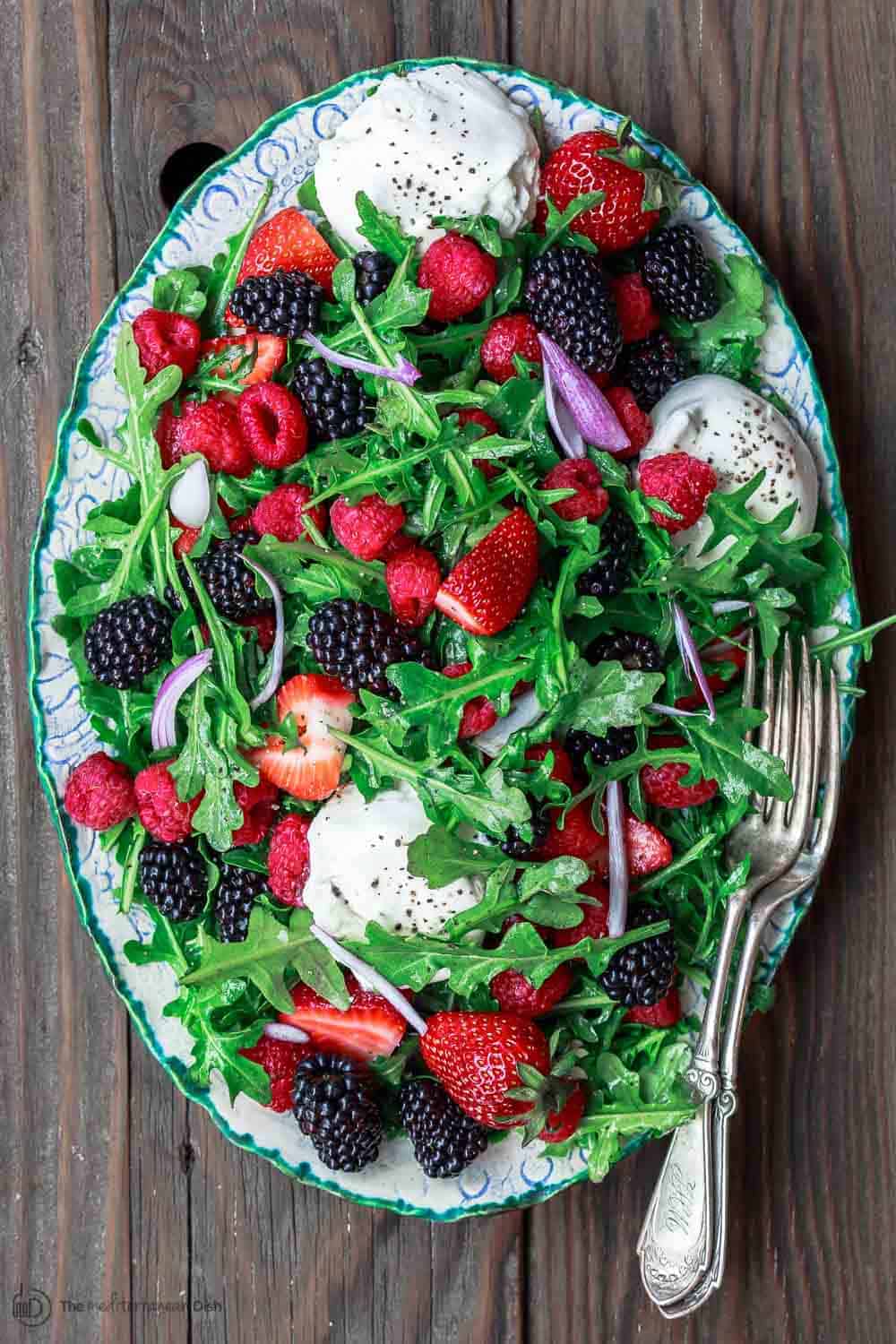 Arugula salad with burrata cheese, raspberries, strawberries and blackberries served in a large plate