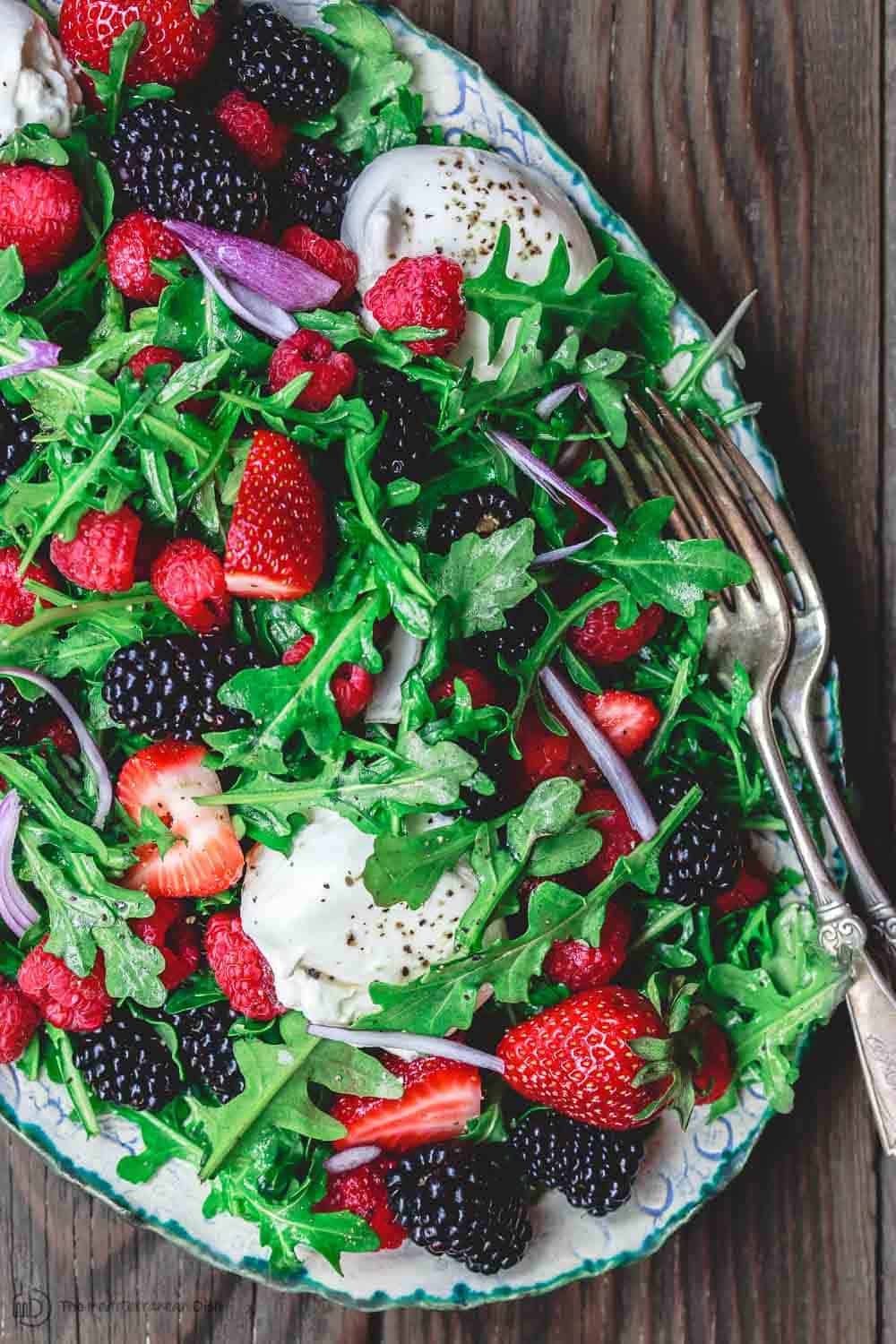 Arugula salad with burrata cheese, raspberries, strawberries and blackberries served in a large plate