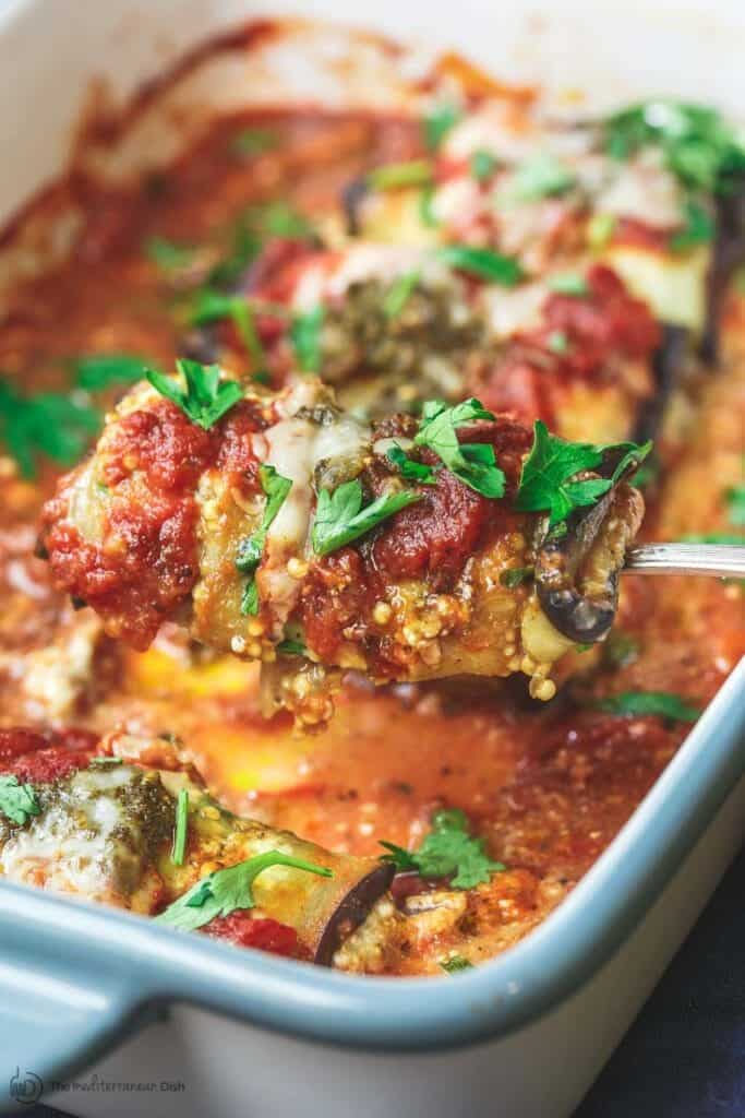 one eggplant rollatini being scooped up from the casserole dish