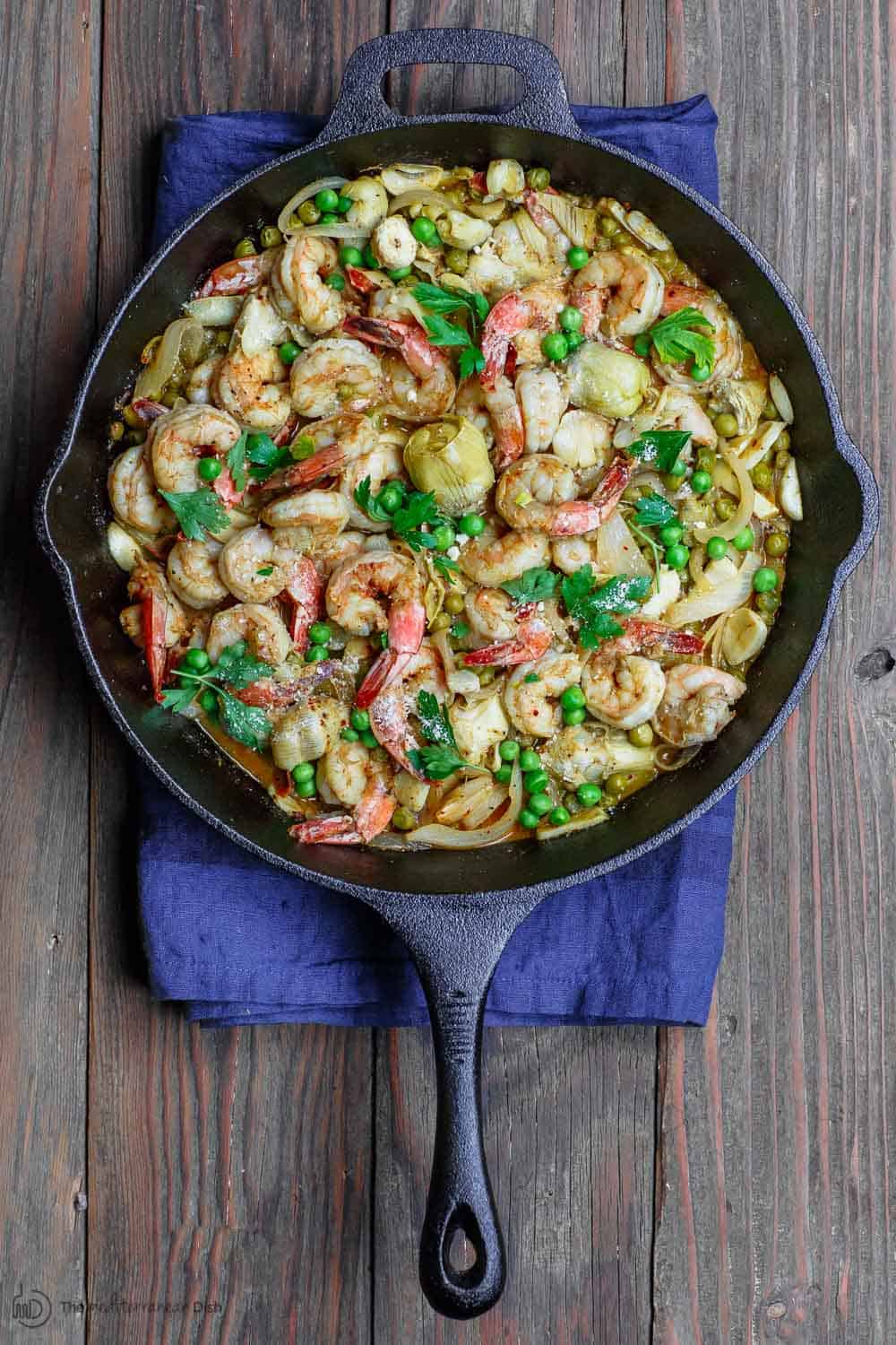 Easy garlic shrimp recipe with peas and artichokes! A quick and bright one-skillet meal. Be sure to see our suggestions for what to serve along. Recipe from TheMediterraneanDish.com #shrimp #glutenfree #mediterraneandiet