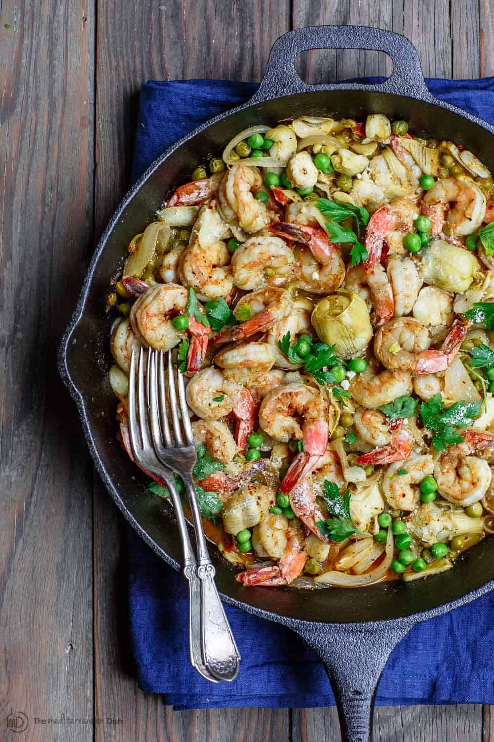 Easy garlic shrimp recipe with peas and artichokes! A quick and bright one-skillet meal. Be sure to see our suggestions for what to serve along. Recipe from TheMediterraneanDish.com #shrimp #glutenfree #mediterraneandiet