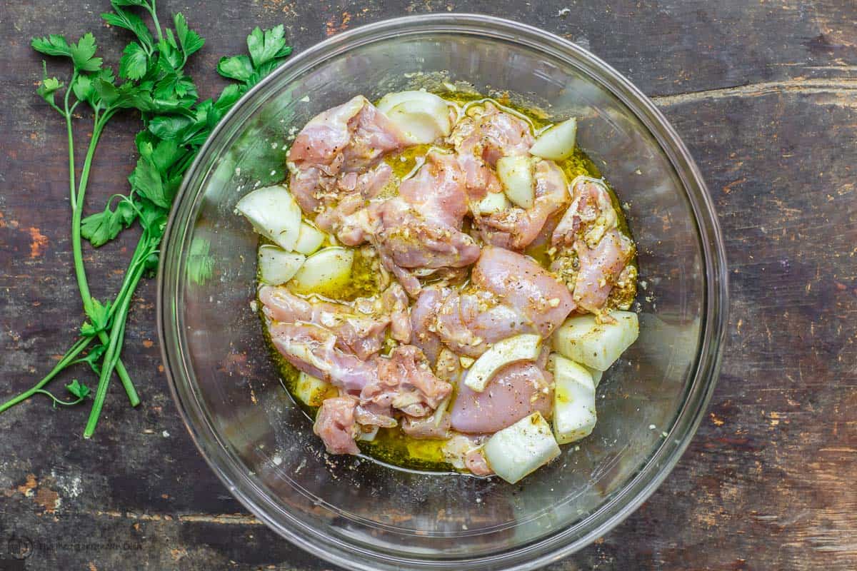 Lemon chicken marinating in a bowl with onions, lemon juice, olive oil, and spices