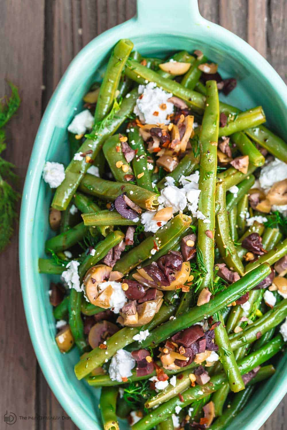 Greek Green Bean Salad Recipe | The Mediterranean Dish. Perfectly tender, flavor-packed green bean salad prepared Greek style. A garlicy, zesty dressing pulls it together, and a sprinkle of feta and chopped marinated olives take it to a new level of delicious. Get the easy recipe on themediterraneandish.com #greenbeans #greekfood #greekrecipe #mediterraneanrecipe #mediterraneandiet