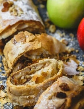 Apple strudel sliced into pieces, some fresh apples to the side
