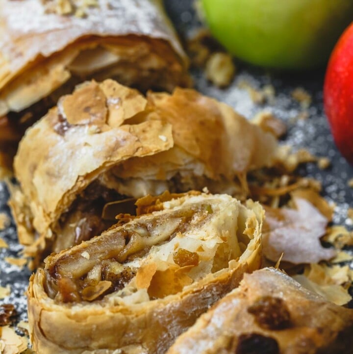 Apple strudel sliced into pieces, some fresh apples to the side