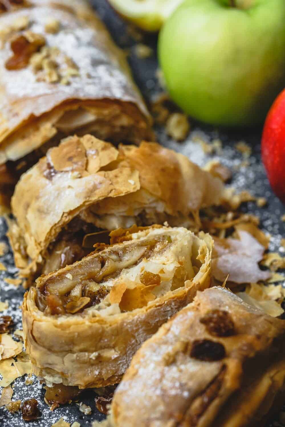 Apple strudel sliced into pieces, some fresh apples to the side