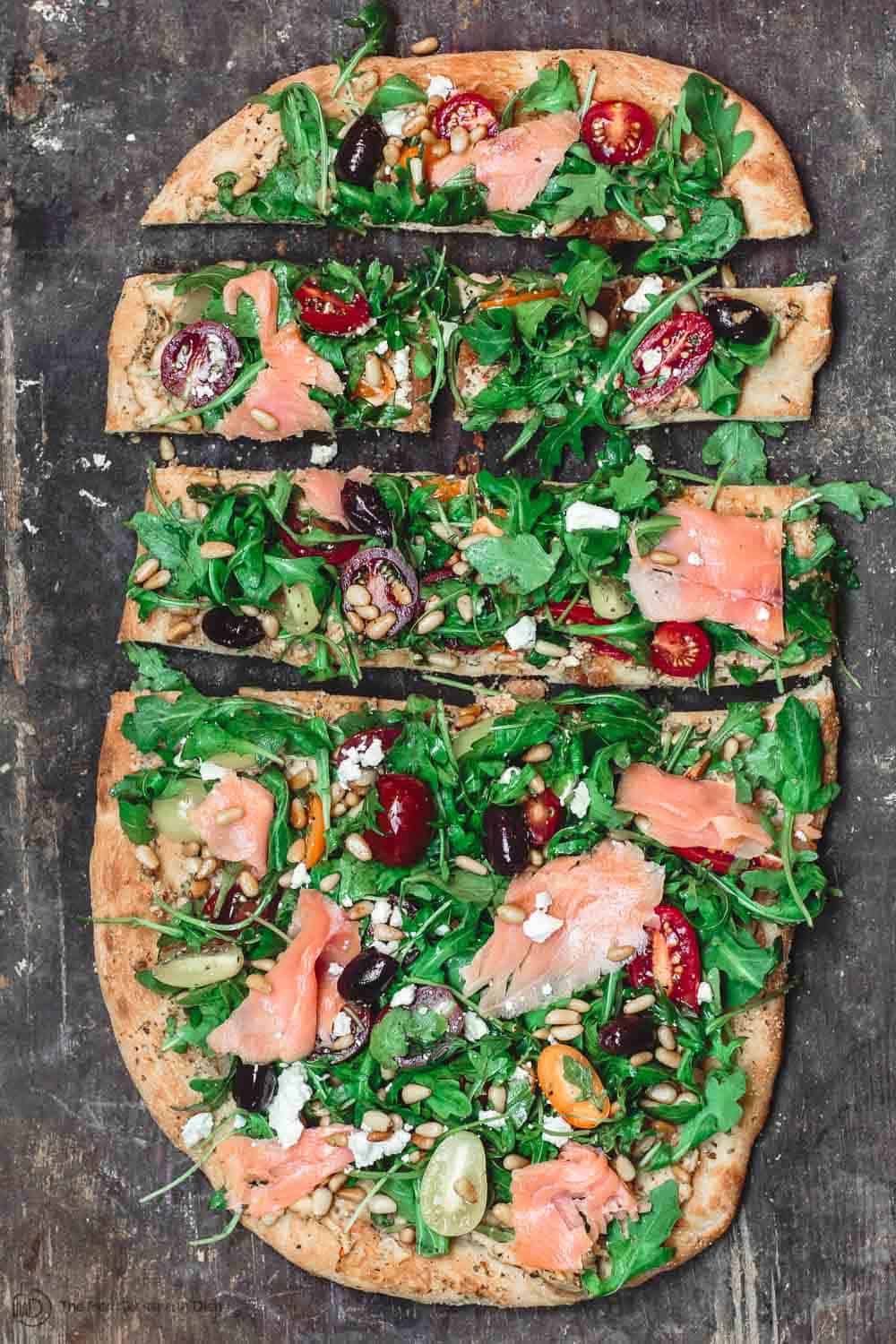 Flatbread with hummus, arugula, tomatoes, smoked salmon and more. Sliced in small pieces to serve as appetizer