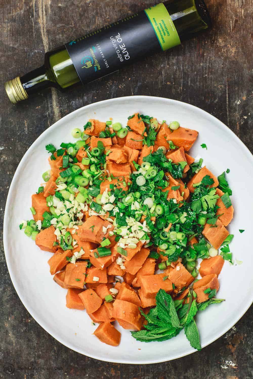 Boiled sweet potato cubes in large mixing bowl with fresh herbs, garlic, and scallions. 