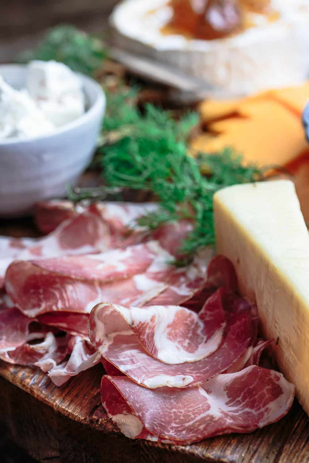 Italian cured meats for a cheese board, hard Parmesan cheese, and a bowl of Greek feta. One corner of a great cheese board.