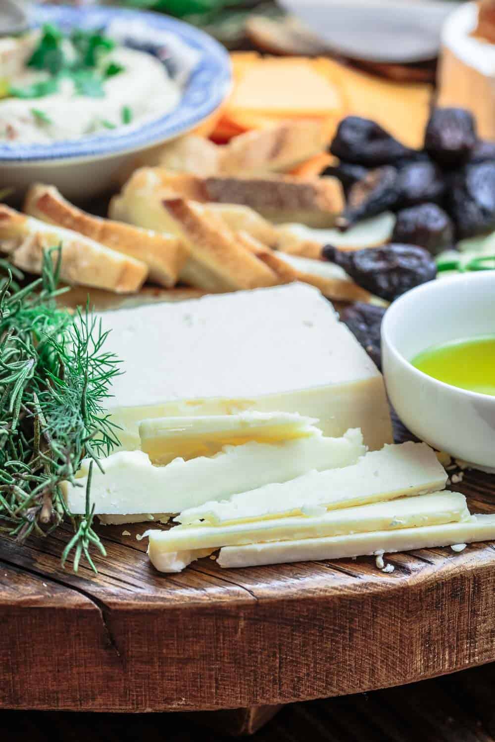 One corner of the best cheese board with sharp cheddar, a bowl of olive oil, dried figs, and sliced banquette