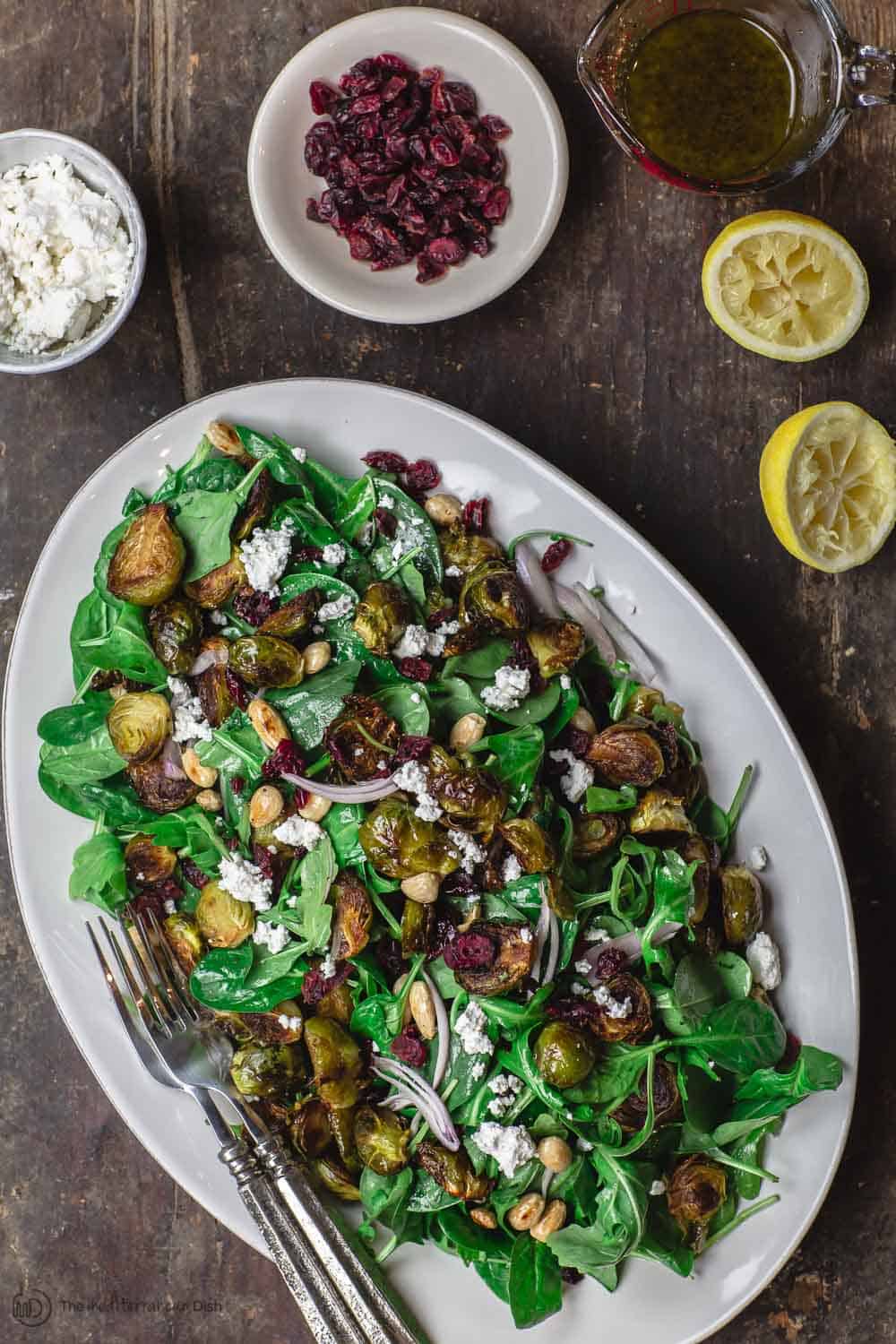 Mediterranean roasted brussels sprouts salad with spinach, arugula, cranberries, almonds and feta. Presented on serving platter with more cranberries and feta cheese on the side.