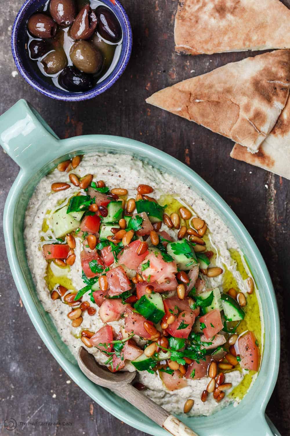 Smoky eggplant dip baba ganoush served with Mediterranean salad on top, pita bread wedges, and a side of olives