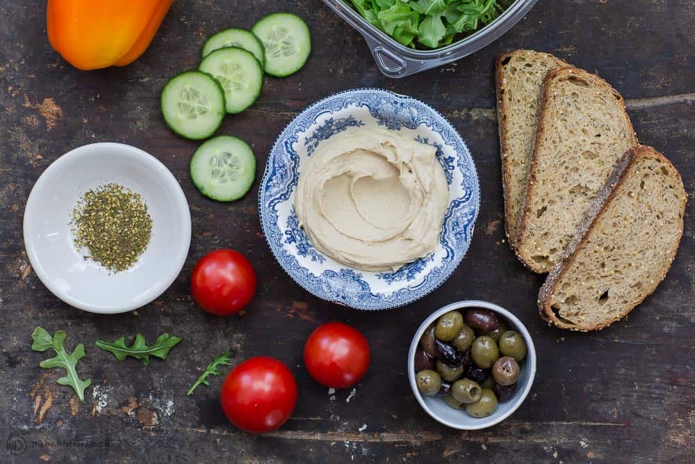Hummus, cucumbers, tomatoes, a bowl of olives, arugula, za'atar spice and whole grain toast. Ingredients for Mediterranean style breakfast toast