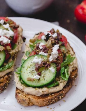 Mediterranean-Style Breakfast Toast with hummus, arugula, cucumbers, tomatoes, olives, a sprinkle of za'atar and feta cheese