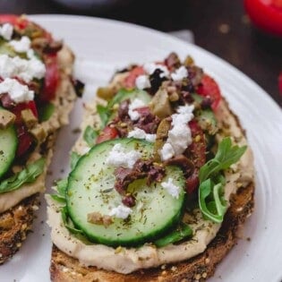 Mediterranean-Style Breakfast Toast with hummus, arugula, cucumbers, tomatoes, olives, a sprinkle of za'atar and feta cheese