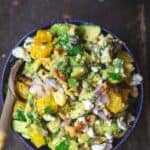 Avocado salsa served in a blue bowl with orange, walnuts, feta, and fresh herbs