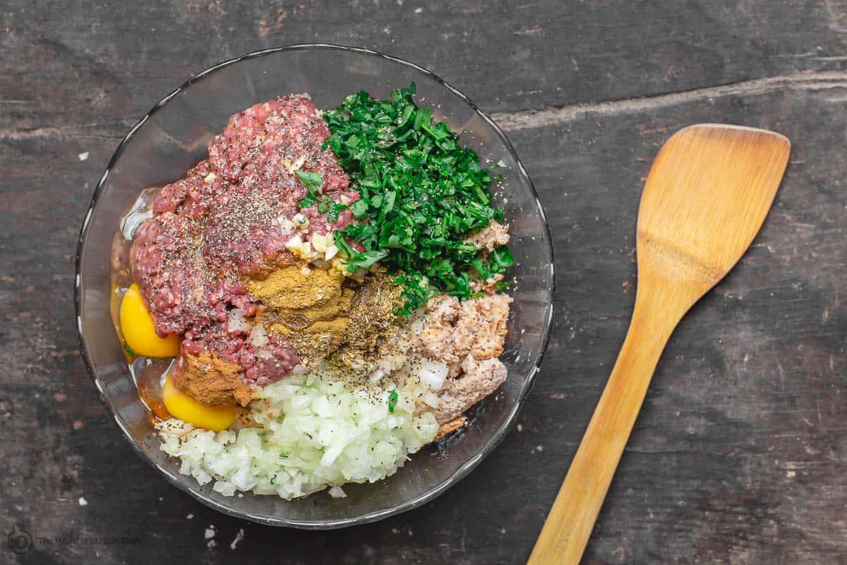 Meatball ingredients in a bowl. Ground beef, onions, garlic, spices, and fresh parsley